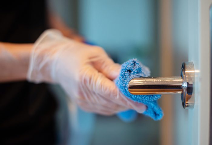 Closeup of the hands of a person disinfecting a door knob