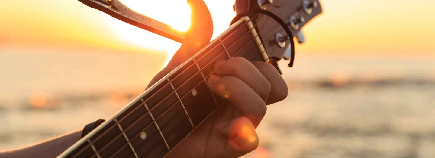 man playing guitar in front of sunset over the sea in devon