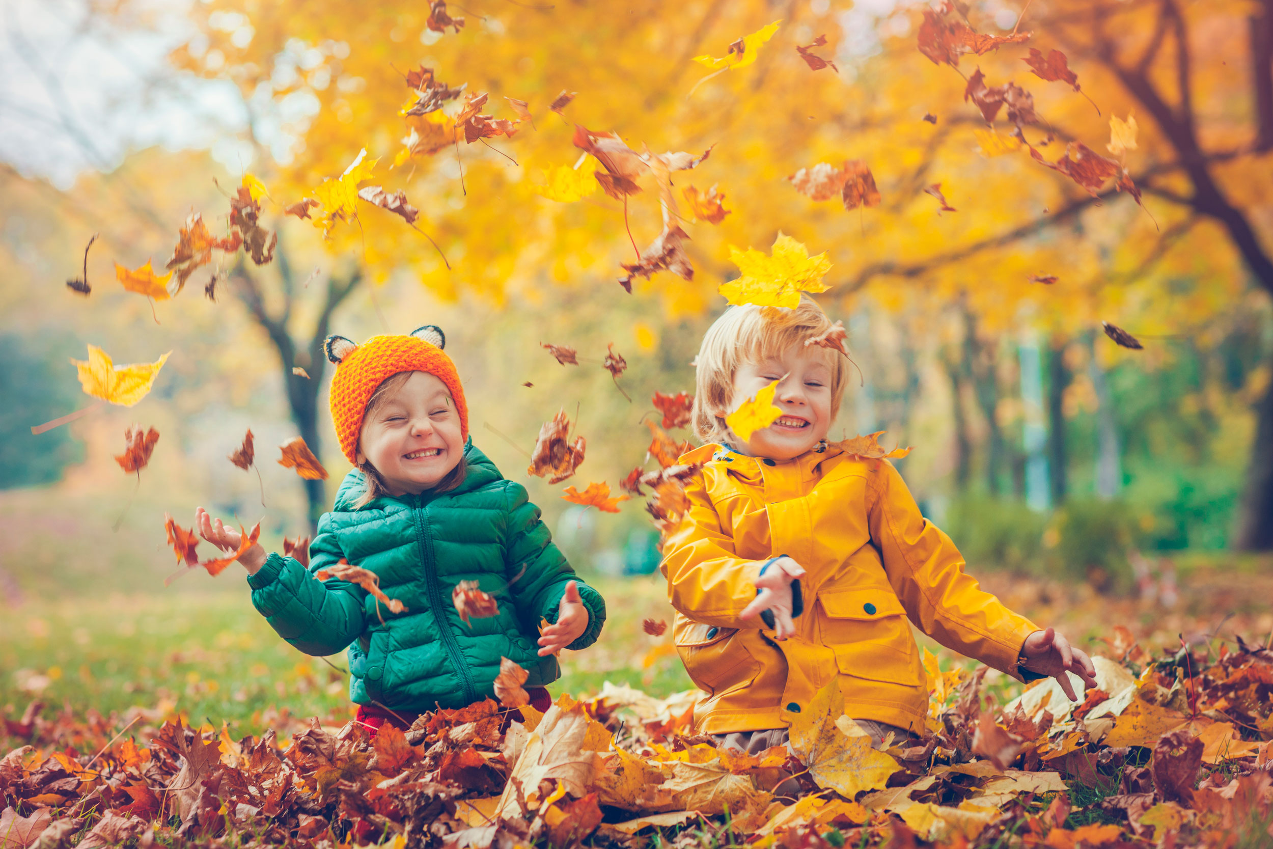 Two young children playing with fallen leaves whilst on Autumn Break in Devon