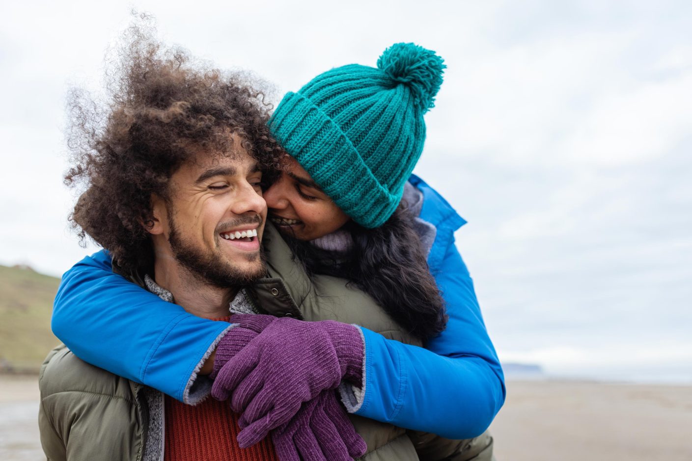 Front view waist up of a mid adult couple enjoying walking along the coast together. It's cold outside so they are wrapped up warm.