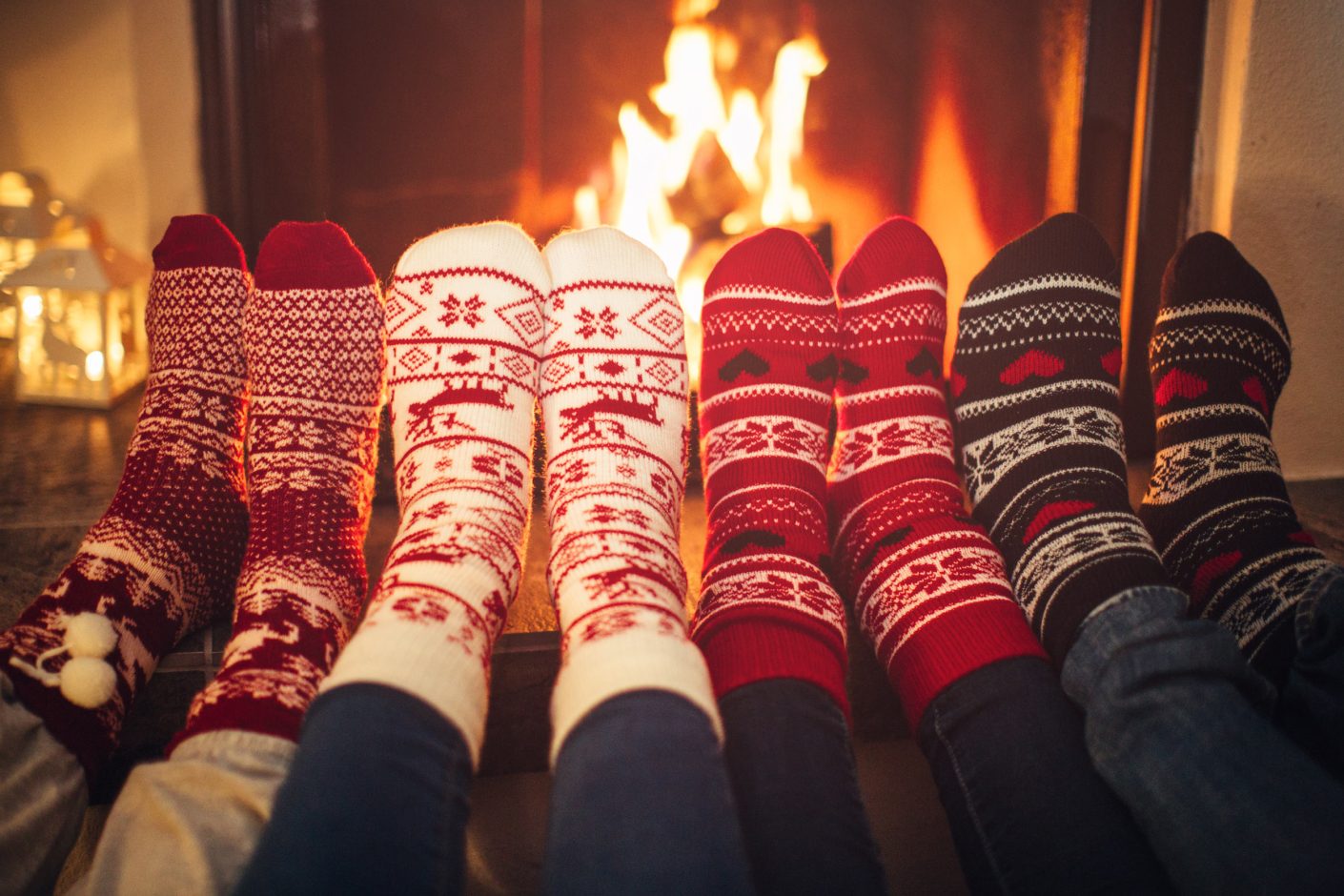 Four pairs of feet wearing christmas socks in front of roaring fire place