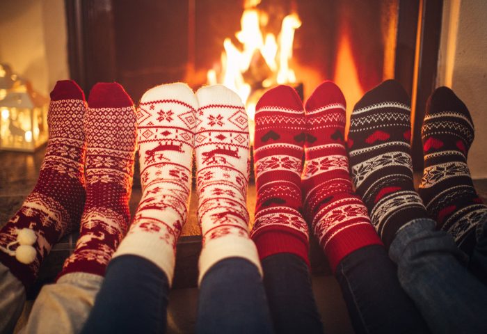 Four pairs of feet wearing christmas socks in front of roaring fire place