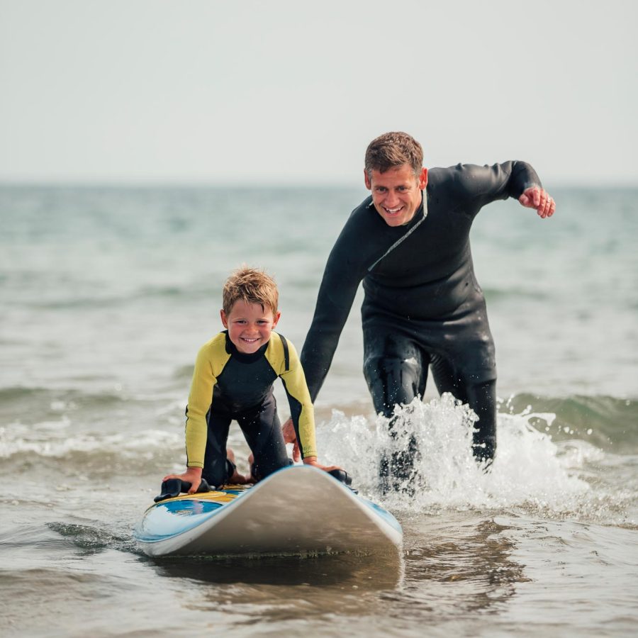 Dad teaching young son to surf on holiday in Woolacombe