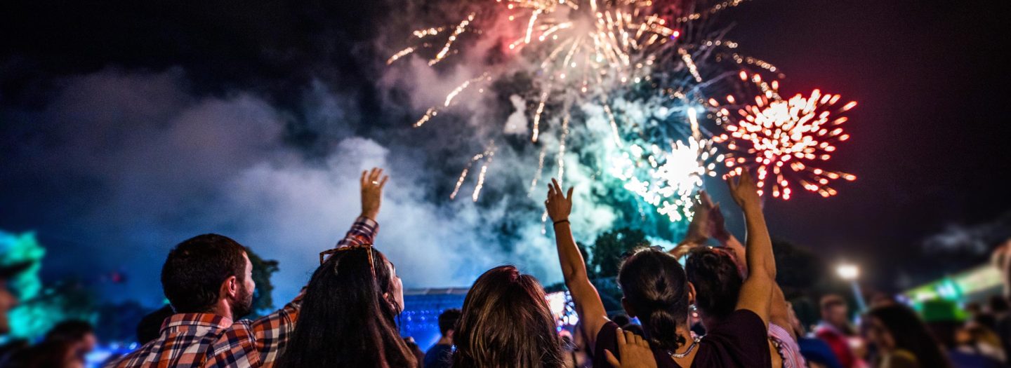 Back view of large group of people watching fireworks on the sky by night.