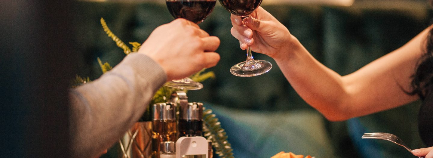 Couple toasting red wine glasses over a romantic meal